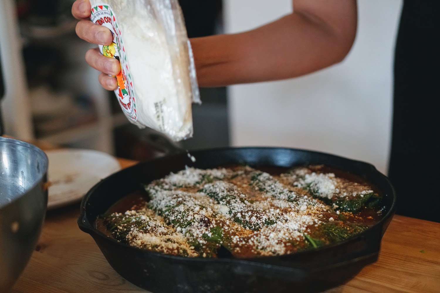 Sprinkling cotija cheese on top of enchiladas in a pan